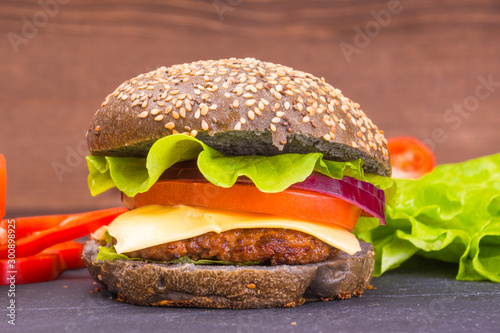 Delicious homemade dark cheese burger with vegetables on a black slate board and chopped ingredients