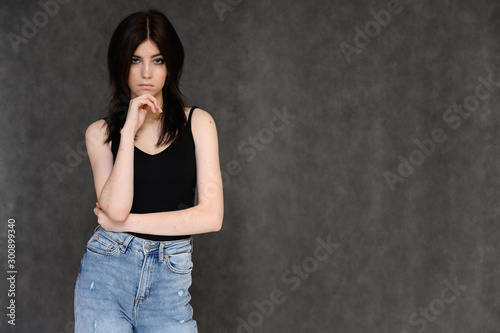 Portrait of a young pretty girl student with long black hair, on a gray background. He stands right in front of the camera, showing his hands in different poses with different emotions.