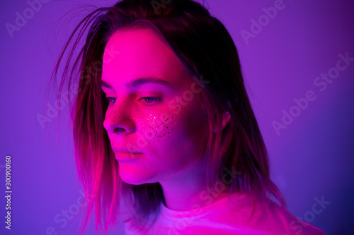Young girl portrait in neon pink and violet lights with glitter freckles on face. Clubber, night life concept. Copy space.