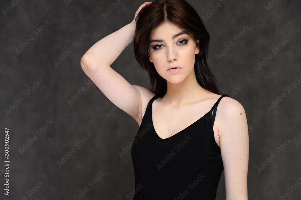Close-up portrait of a young pretty girl student with long black hair, on a gray background. He stands right in front of the camera, showing his hands in different poses with different emotions. Close-up portrait of a young pretty girl student with long black hair, on a gray background. He stands right in front of the camera, showing his hands in different poses with different emotions.