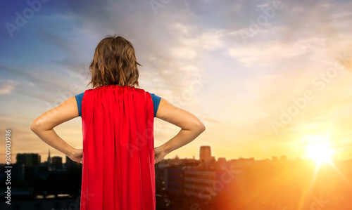 women's power and people concept - back view of young woman in red superhero cape over sunset in tallinn city background