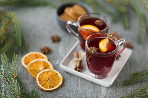 christmas and seasonal drinks concept - hot mulled wine, dry orange slices, gingerbread and aromatic spices on grey background