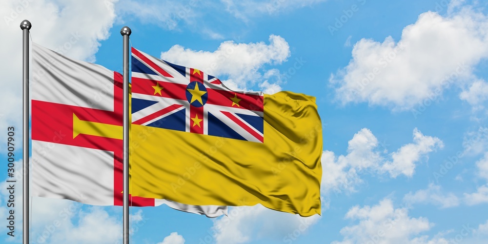Guernsey and Niue flag waving in the wind against white cloudy blue sky together. Diplomacy concept, international relations.