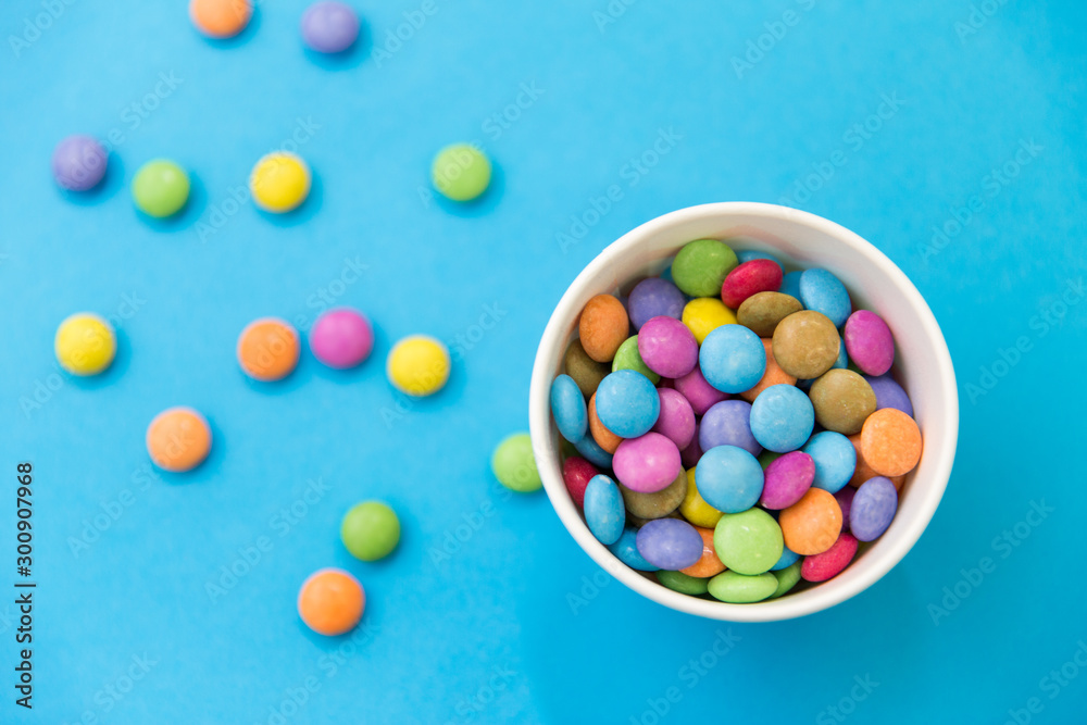food, confectionery and sweets concept - candy drops in paper cup on blue background