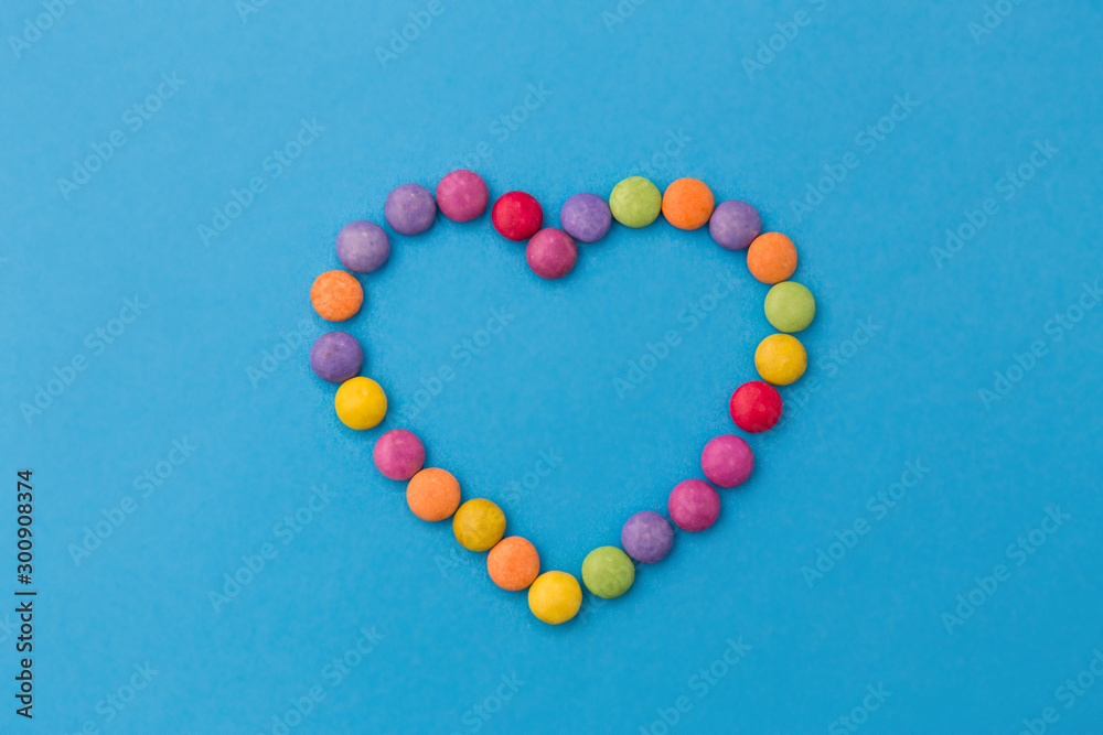 sweets, confectionery and valentine's day concept - bright multicolored candy drops in shape of heart on blue background - obrazy, fototapety, plakaty 