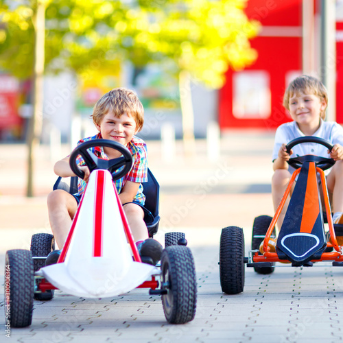 Two active little kid boys driving pedal race car in summer garden, outdoors. Children, best friends racing with fast speed and having fun. Twins making competition. photo