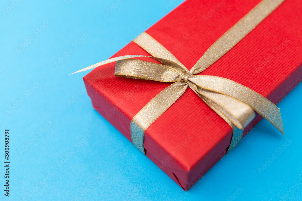 Fototapeta premium holiday, greeting and surprise concept - christmas red gift box with golden bow on blue background