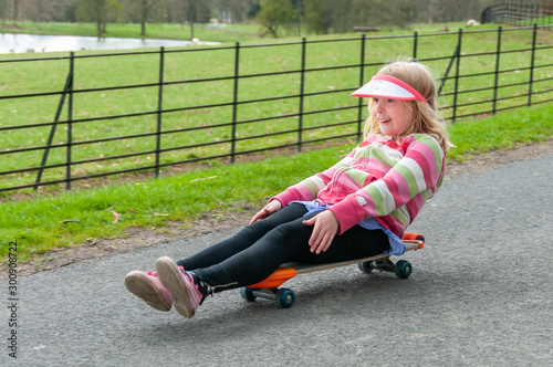 Excited and very happy young blonde girl riding a skateboard in a rural setting