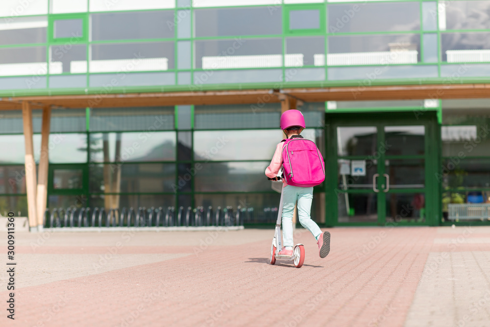 education, childhood and people concept - school girl with backpack riding scooter