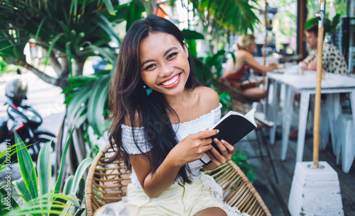 Playful beautiful Asian woman reading book in street cafe