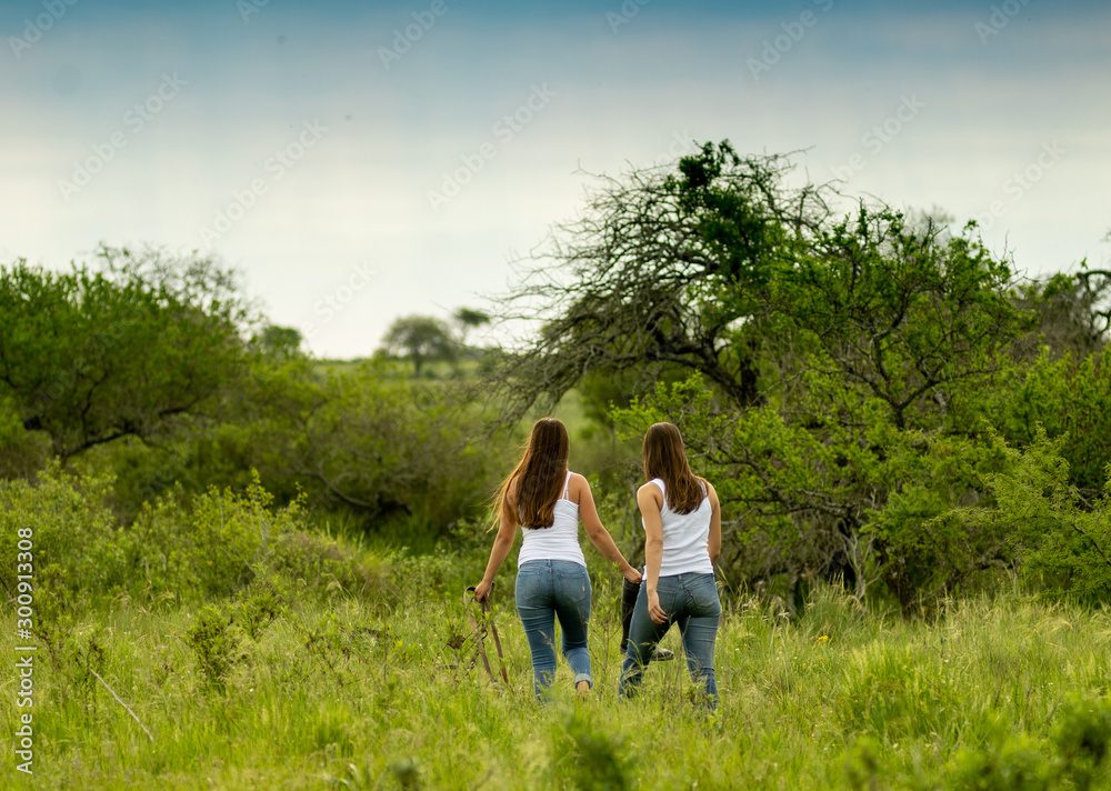 Young female sisters walk in the field, looking for the horses to ride