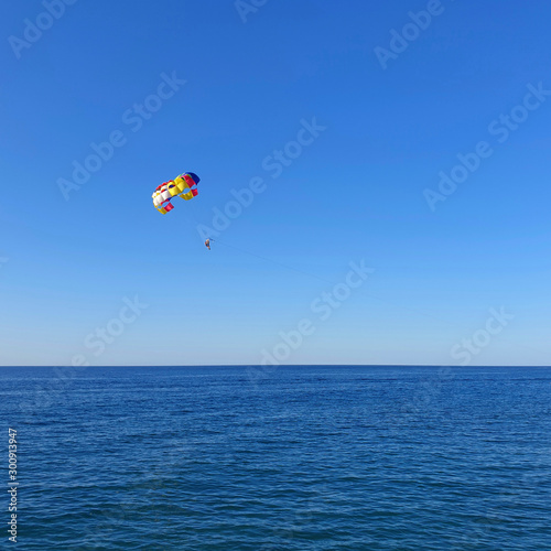 A man with a parachute flies over the sea.