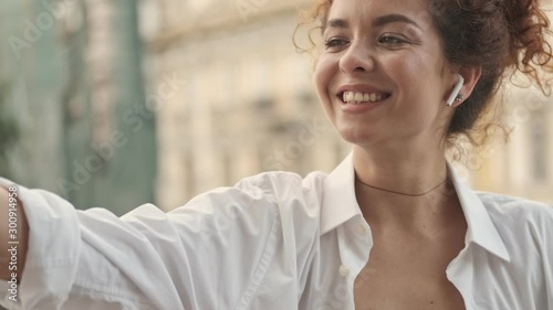 Close up view of attractive happy young redhead woman in white shirt smiling and taking selfie photo on smartphone while relaxing on the balcony at home in the morning photo