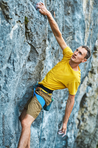 Young strong man climbing challenging route on a high vertical limestone cliff, resting and considers route. Conquering, overcoming and active lifestyle concept.