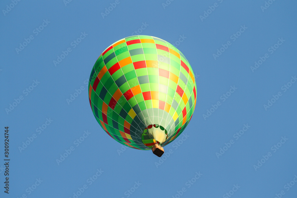 Fototapeta premium Green hot air balloon flying over the small city in a clear blue sky.