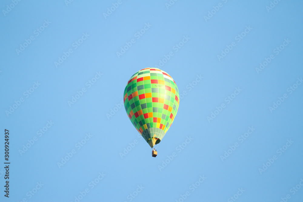 Green hot air balloon flying over the small city in a clear blue sky.