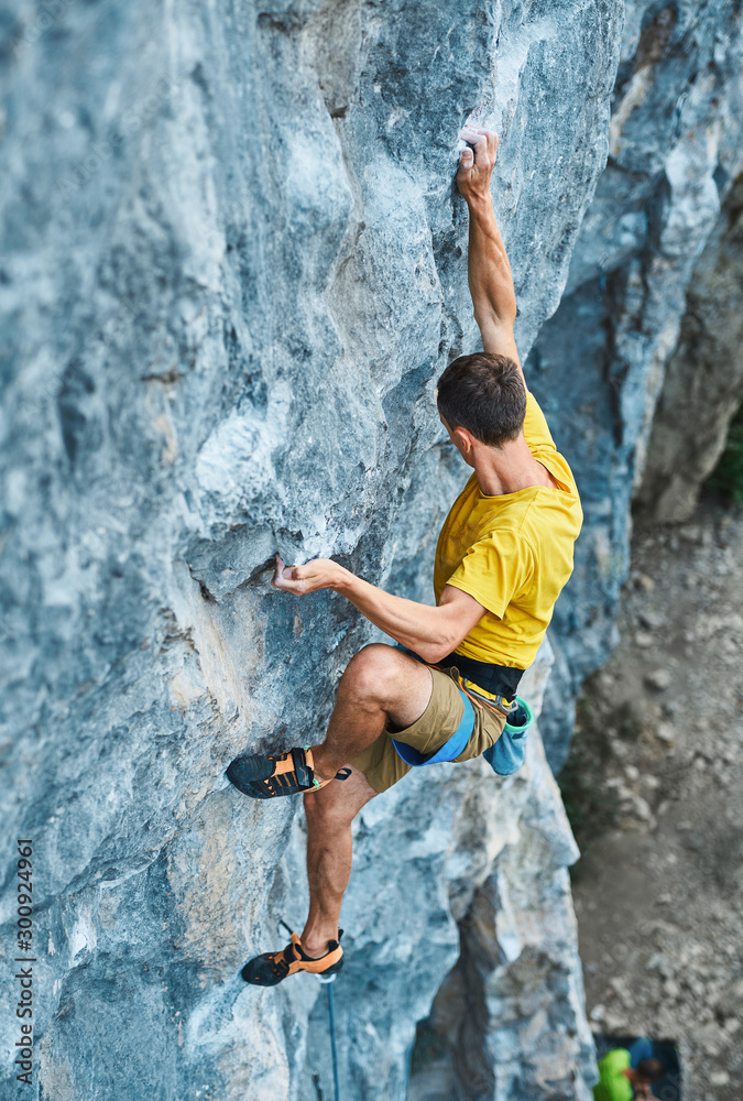young strong man rock climber climbing on a high vertical limestone cliff, reaching holds, making hard wide move and gripping hold, attaching rope. Conquering, overcoming and active lifestyle concept. young strong man rock climber climbing on a high vertical limestone cliff, reaching holds, making hard wide move and gripping hold, attaching rope. Conquering, overcoming and active lifestyle concept.