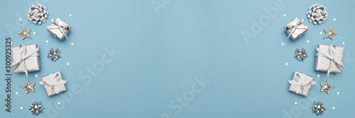 Gifts or present boxes in silver with silver bows and tree ball ornaments and little silver stars, table tob view. Composition for Christmas. Blue pastel background.