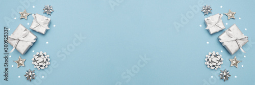 Gifts or present boxes in silver with silver bows and tree ball ornaments and little silver stars, table tob view. Composition for Christmas. Blue pastel background.