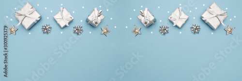 Gifts or present boxes in silver with silver bows and tree ball ornaments and little silver stars, table tob view. Composition for Christmas. Blue pastel background.