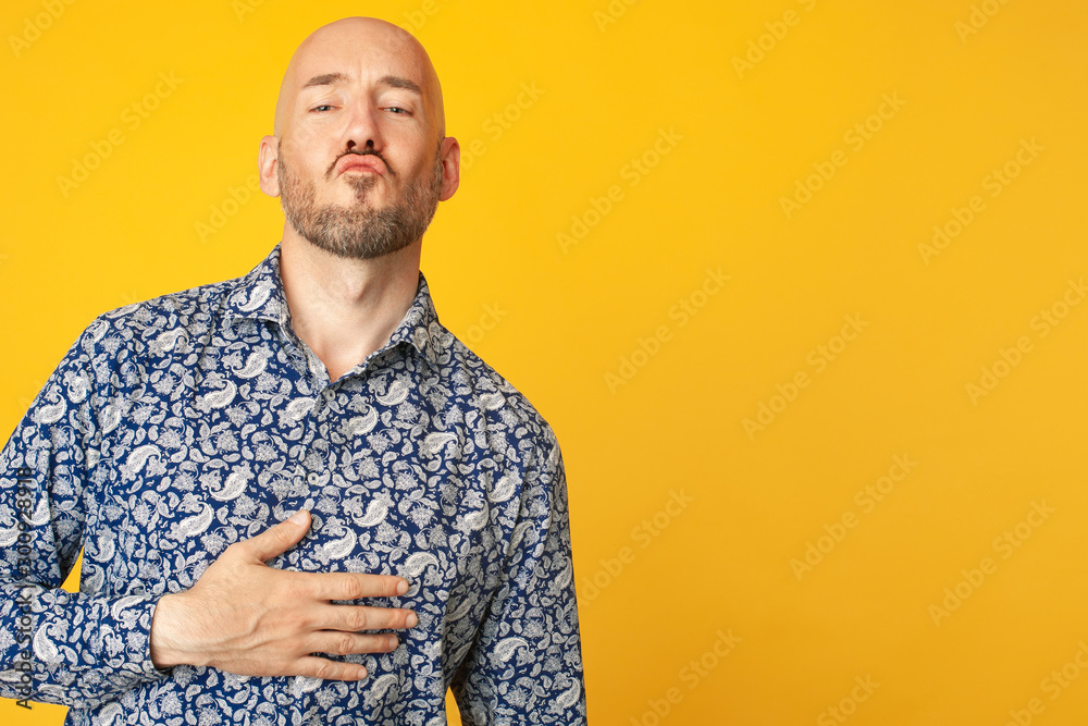 Fabulous at any age. Portrait of 40-year-old man sending air kiss over light yellow background in blue shirt. Funny face. Hipster style. Bald shaved head. Copy-space. Close up. Studio shot Stock Photo | Fabulous at any age. Portrait of 40-year-old man sending air kiss over light yellow background in blue shirt. Funny face. Hipster style. Bald shaved head. Copy-space. Close up. Studio shot Stock Photo |