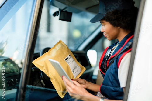 African American courier checking address on a package while using touchpad in delivery van. photo