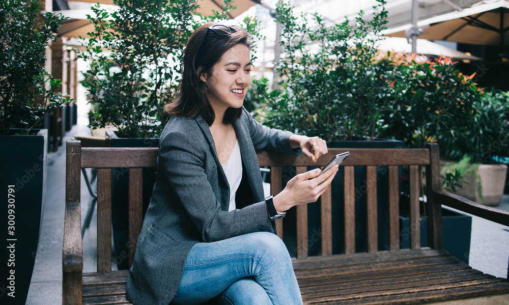 Happy woman using smartphone while sitting on bench