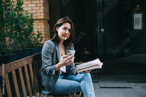 Content female messaging on mobile and resting on bench with notebook