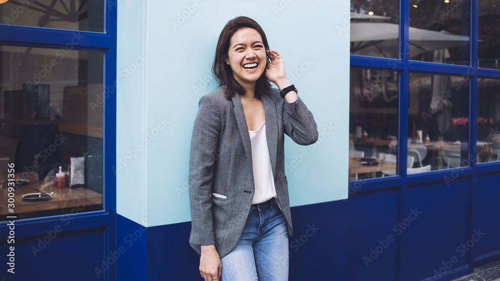 Happy Asian female millennial leaning against wall on street