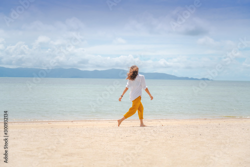 Young beautiful woman in a white shirt and yellow pants runs joyfully on the beach along the sandy shore of a tropical sea