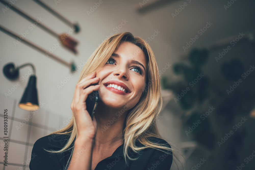 Fototapeta premium Happy hipster girl in casual wear phoning to friend via smartphone gadget feeling good during communication, positive female teenager with blonde hair using mobile application for making conversation