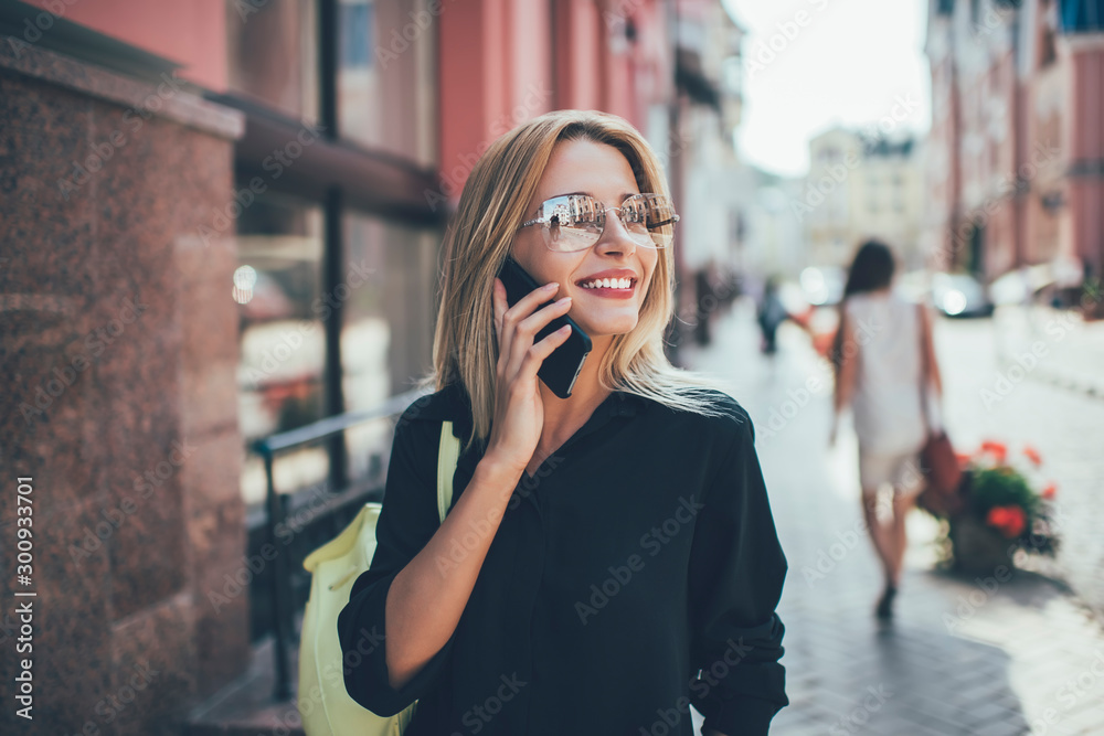 Successful hipster girl in trendy sunglasses rejoicing during international conversation with friend connected to roaming in trip, positive Caucasian tourist smiling while receiving good news