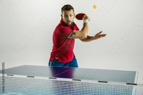 Overcoming. Young man plays table tennis on white studio background. Model plays ping pong. Concept of leisure activity, sport, human emotions in gameplay, healthy lifestyle, motion, action, movement. photo