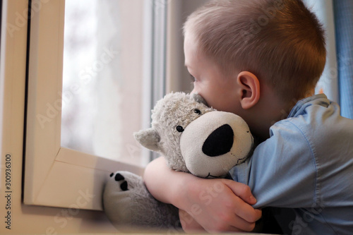 Sad boy at the window and bear toy, loneliness and depression photo