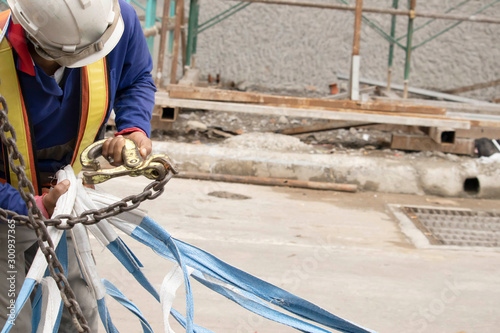 Workers wear white hats, blue jackets and reflective clothing, fastening the strap to the crane's steel hooks to lift items upstairs.