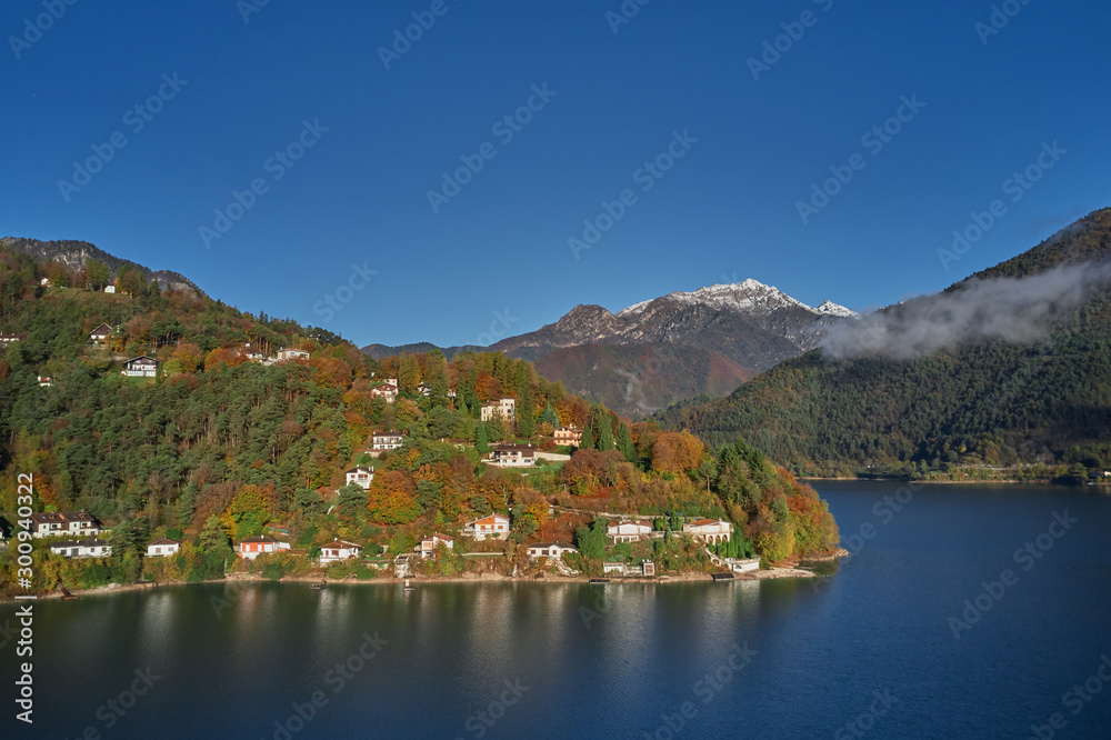 Panoramic view of the mountains and lake Pieve di Ledro, Italy. Autumn season, the reflection in the water of the mountains, trees, blue sky