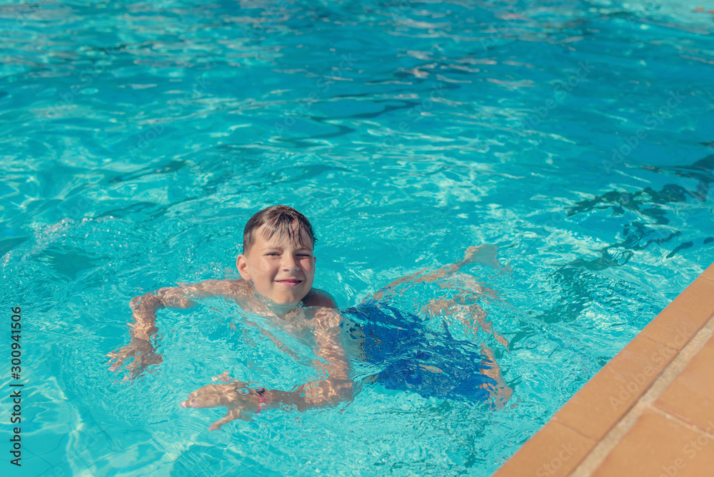 Portrait of Caucasian boy in swimming pool at resort. He is smiling and looking into camera.