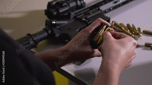 Young Female Reloading Rifle Bullets into a Magazine while Rifle and Bullets Sit on the Table Beside her Inside a Shooting Range in Slow Motion