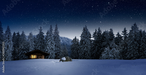 Gemütliche Holzhütte mit Beleuchtetem Fenster in Wnterwald bei Nacht im Winter photo