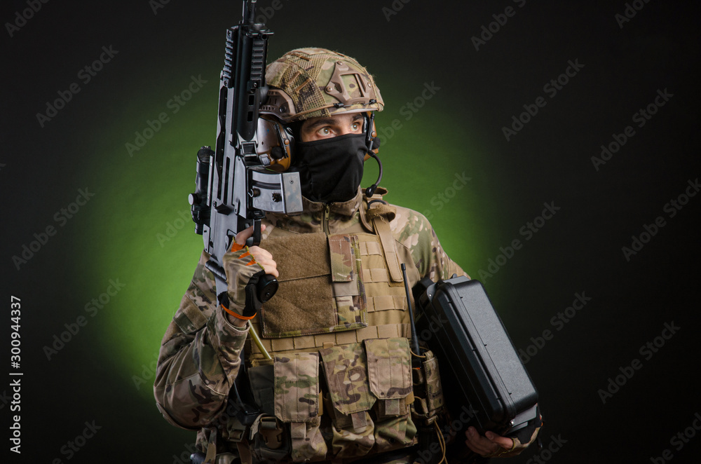 Fototapeta premium a male soldier in military clothes with a weapon on a dark background