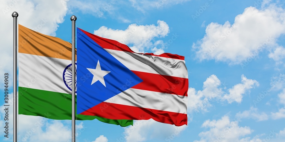 India and Puerto Rico flag waving in the wind against white cloudy blue sky together. Diplomacy concept, international relations.