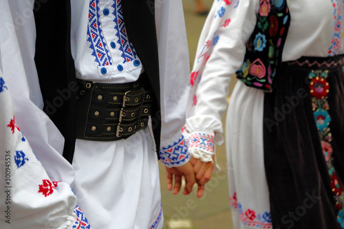 Dancers hold hands in a traditional Romanian dance wearing traditional beautiful costumes.