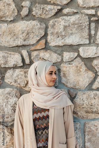 portrait of young European Muslim women with hijab. Stone wall is in her background. She is happy and relaxed.