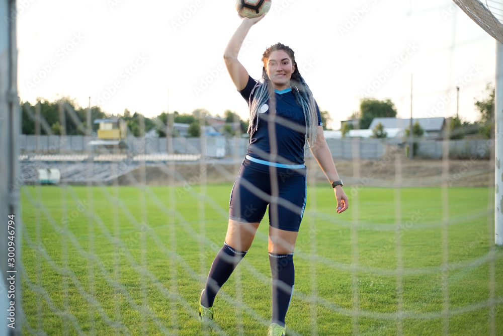 woman with the ball in her hands, on the green grass, football field, through the net gate