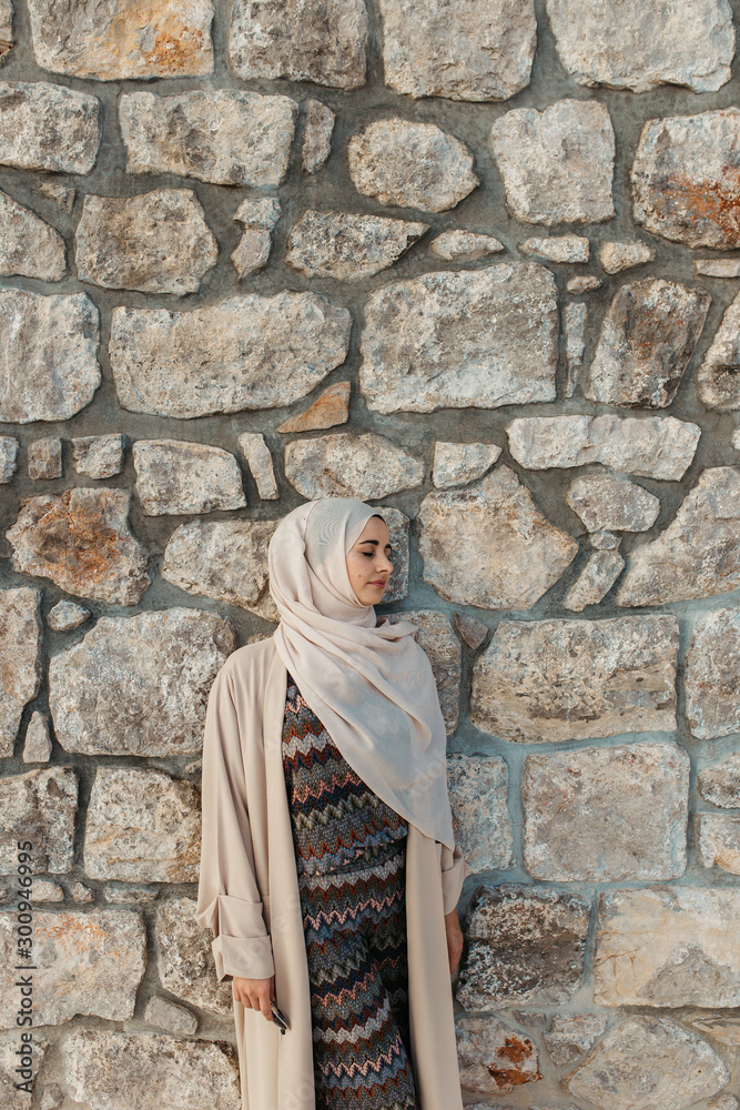 portrait of young European Muslim women with hijab. Stone wall is in her background. She is happy and relaxed. portrait of young European Muslim women with hijab. Stone wall is in her background. She is happy and relaxed.