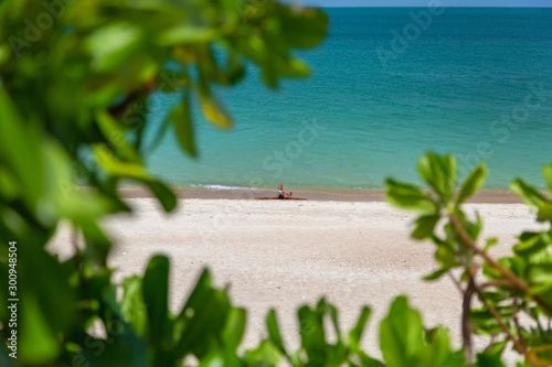 A tanned man lies on the beach of the Gulf of Thailand in the afternoon in the sun, on the edges of a vignette of green plants