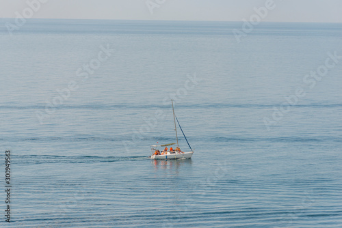 Aerial view on a white floating sailboat with people in it in the blue black sea