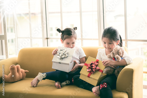 A 6 and 4 year old Asian girl Sitting on yellow sofa, are happiness and excited Because received a pleasant gift On the New Year's Day festival, to children and holiday concept. photo