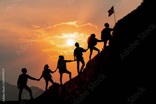 Silhouette of people helping each other hike up a mountain at sunset background. Hiking, Business, teamwork, success, help and goal concept. photo