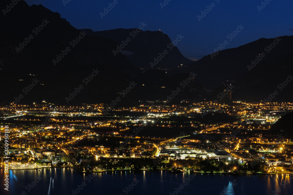 Evening panoramic view of the of Riva Del Garda, Lake Garda. City night lights reflected in water. Aerial view of the city of Riva del Garda